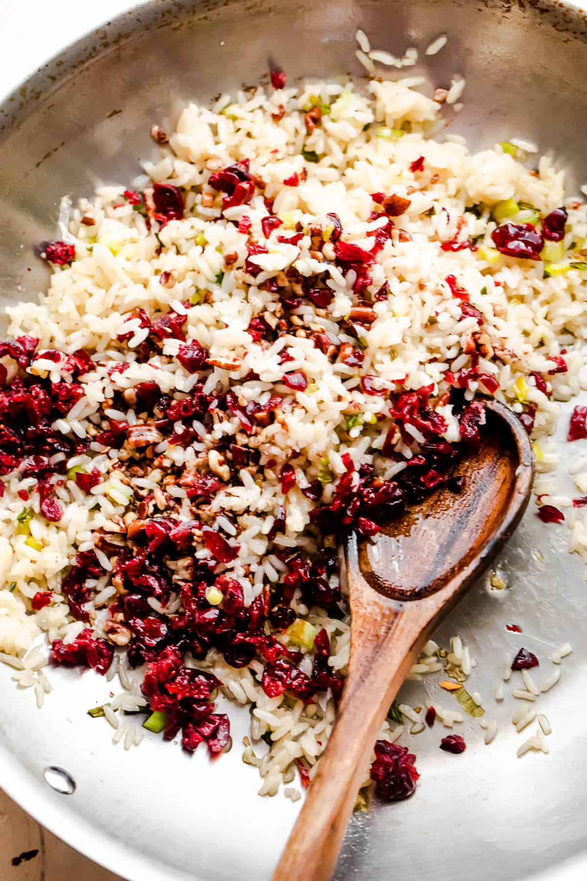 rice and cranberries mixture in a skillet and a wooden spoon stirring through.