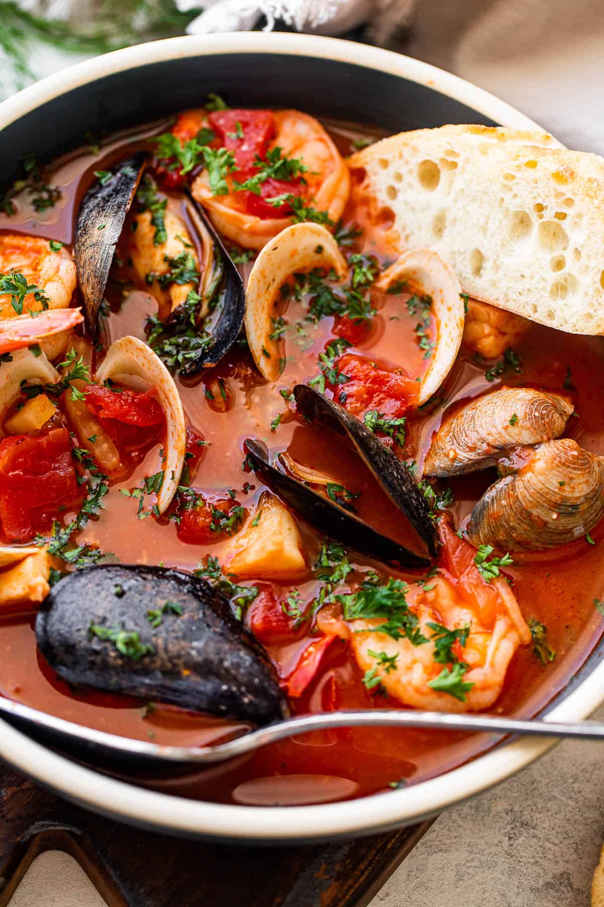 seafood tomato stew in a blue soup bowl served with a slice of crusty bread and a spoon