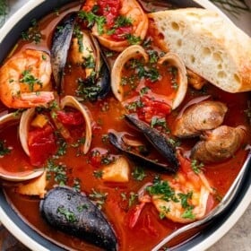 overhead photo of a blue bowl with tomato stew and mussels, clams, cod, and shrimp served with a slice of bread