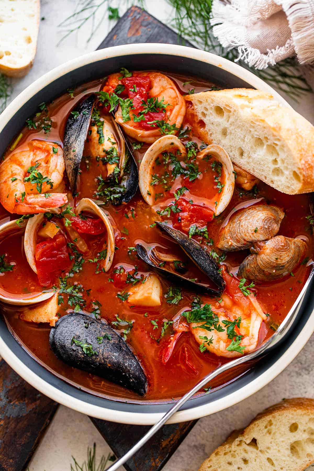 overhead photo of a blue bowl with tomato stew and mussels, clams, cod, and shrimp served with a slice of bread