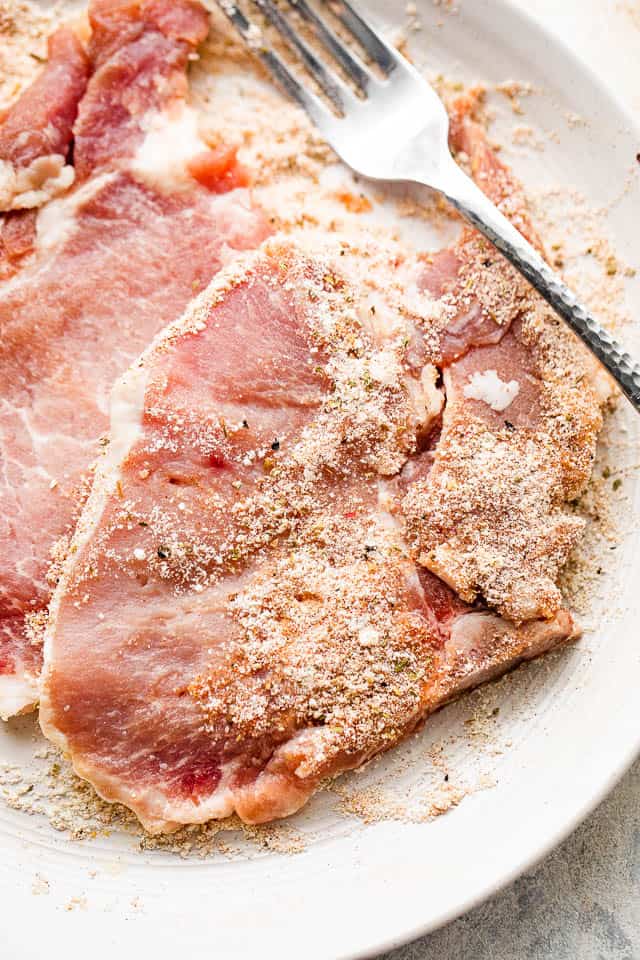 raw pork chops on a plate with a fork to the side