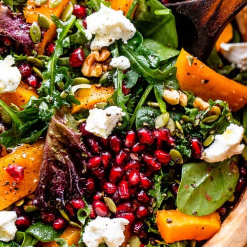 close up shot of salad greens topped with squash, pomegranate arils, nuts, and goat cheese