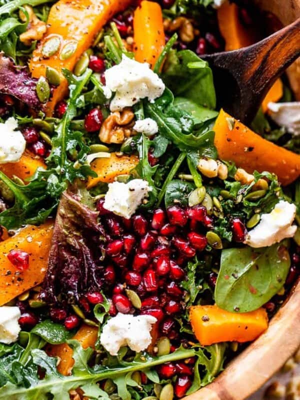 close up shot of salad greens topped with squash, pomegranate arils, nuts, and goat cheese
