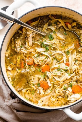 overhead shot of chicken noodle soup in a white dutch oven with a ladle inside the pot
