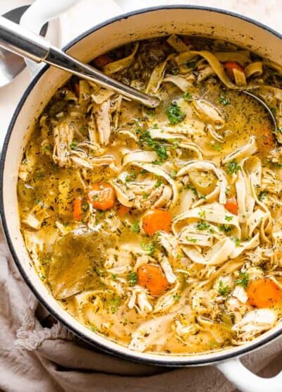 overhead shot of chicken noodle soup in a white dutch oven with a ladle inside the pot