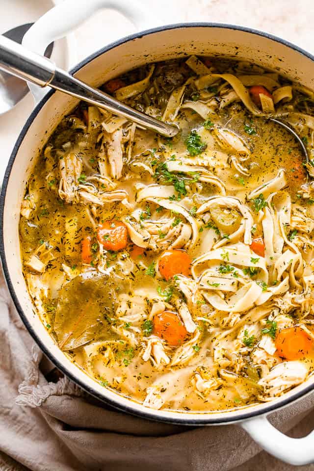 Overhead photo of chicken noodle soup in a white Dutch oven with a ladle placed inside the pot.