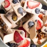 overhead shot of low carb cheesecake bites on a stick and arranged in a white bowl and topped with berries