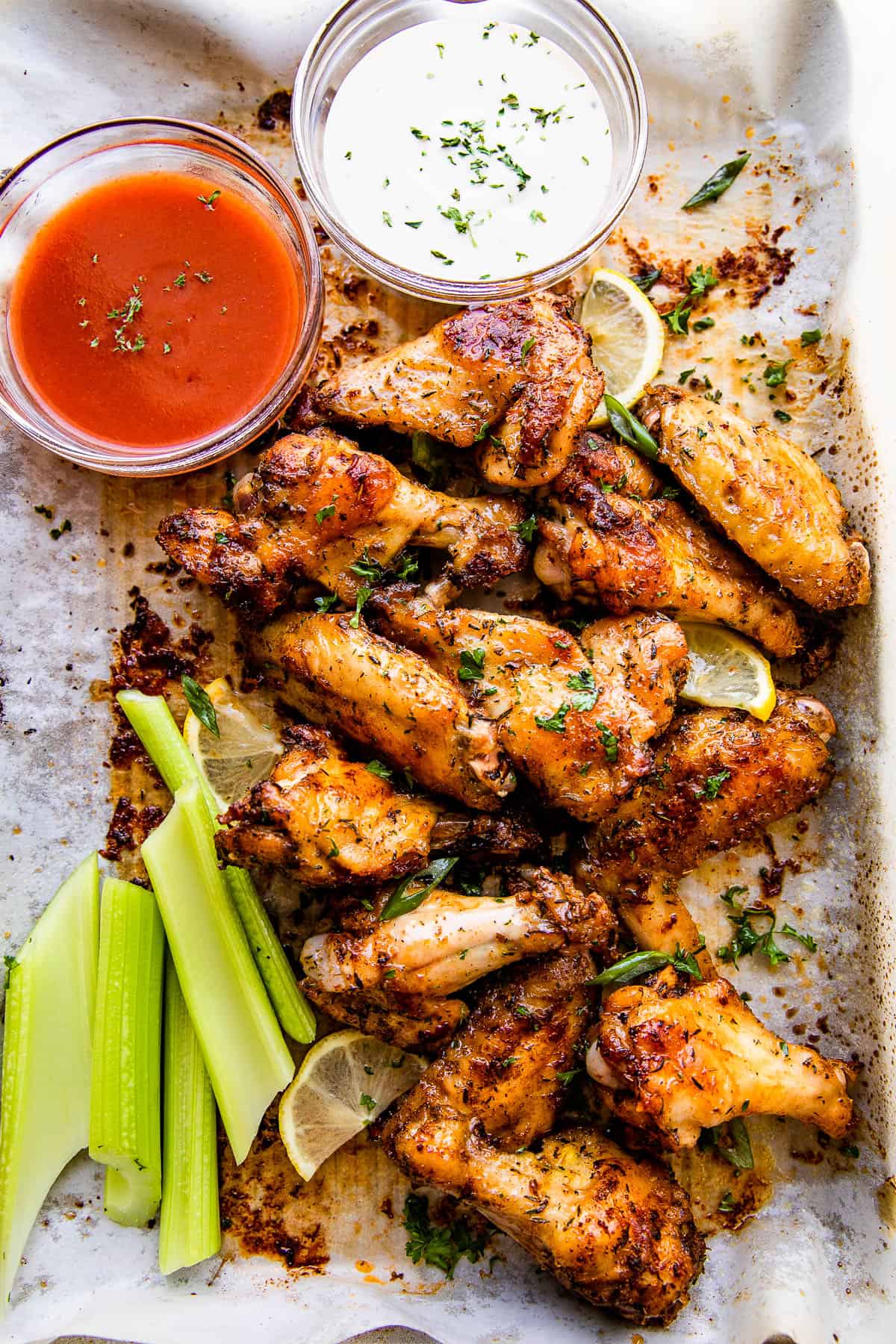 overhead picture of chicken wings on a platter served with sriracha sauce, ranch, and celery sticks.