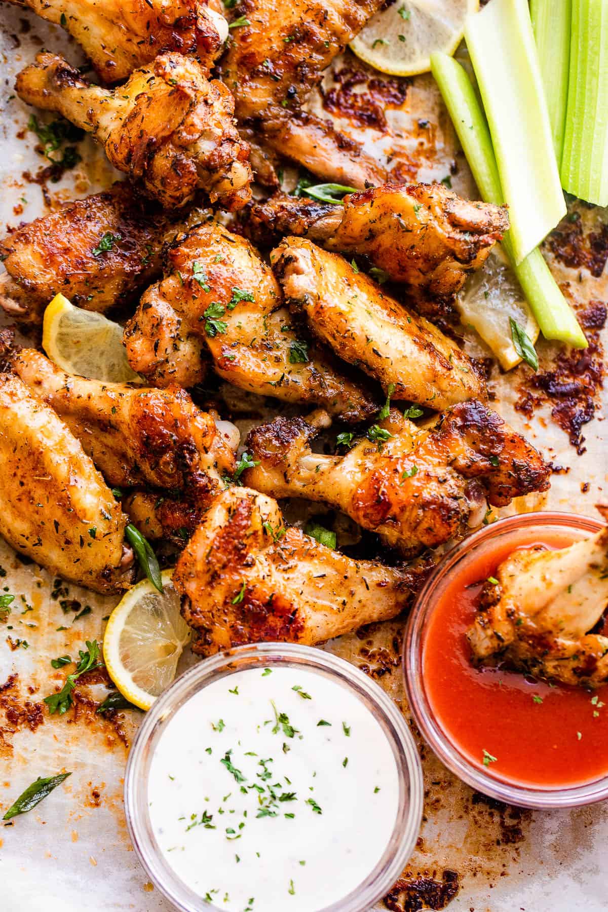 chicken wings on a platter served with sriracha sauce, ranch, and celery sticks.