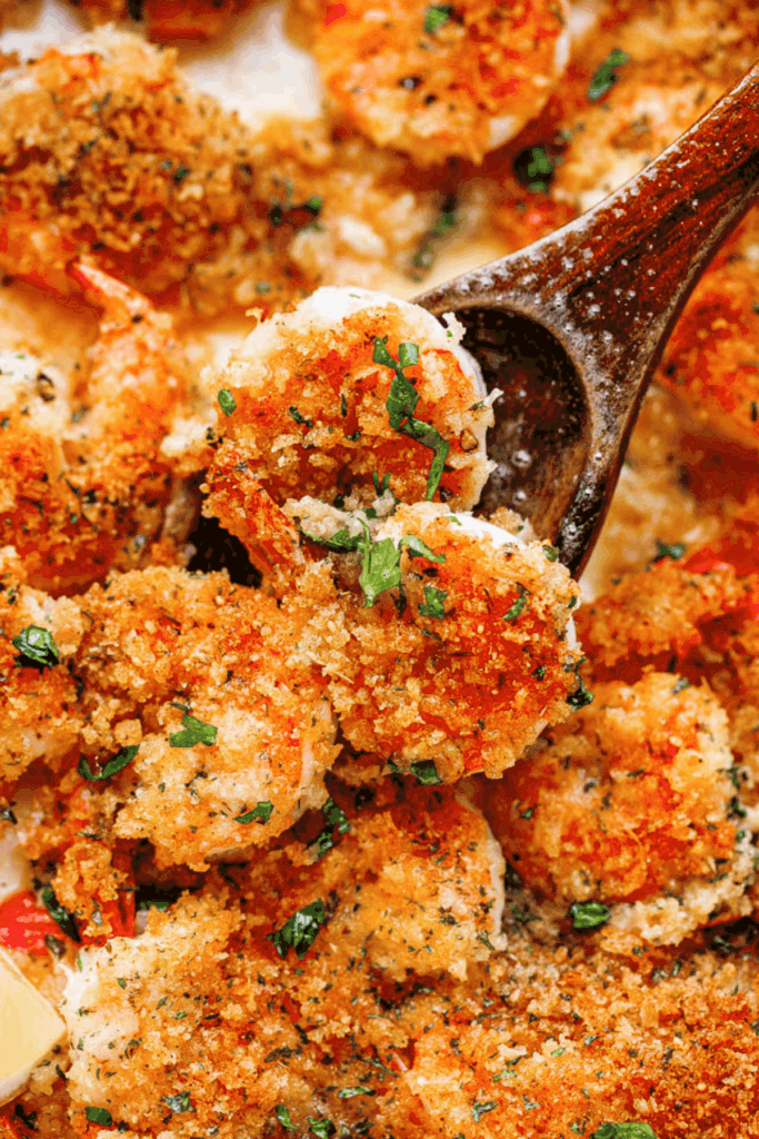 Close-up image of baked shrimp scampi scooped up with a wooden spoon.