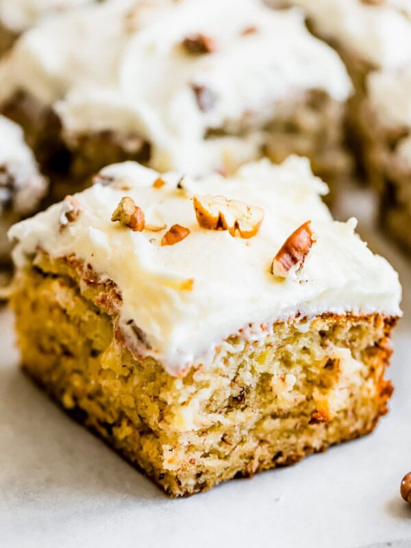 A square of banana cake frosted with cream cheese and topped with chopped pecans.