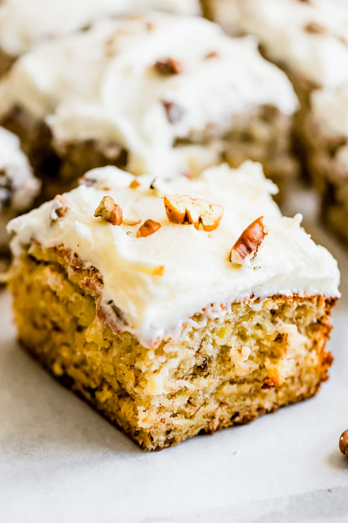 A square of banana cake frosted with cream cheese and topped with chopped pecans.