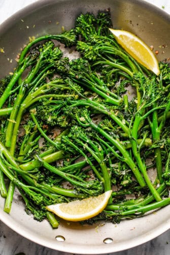 closeup shot of sauteed broccolini served with lemon wedges