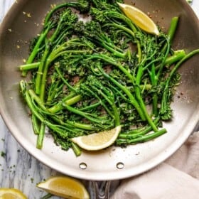 overhead shot of sauteed broccolini and lemon wedges pictured in a stainless steel skillet