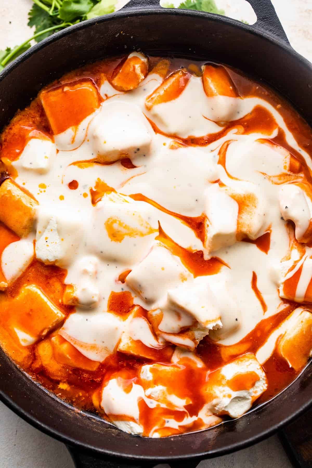 cubed cream cheese, hot buffalo sauce, and ranch dressing cooking in a cast iron skillet