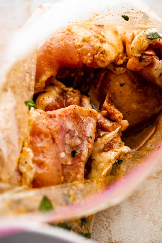 Chicken thighs soaking in marinade inside a ziploc bag.