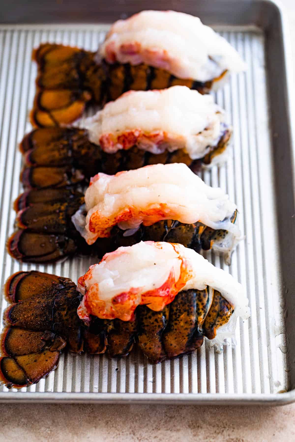 Four Freshly Thawed Lobster Tails on a Metal Baking Sheet