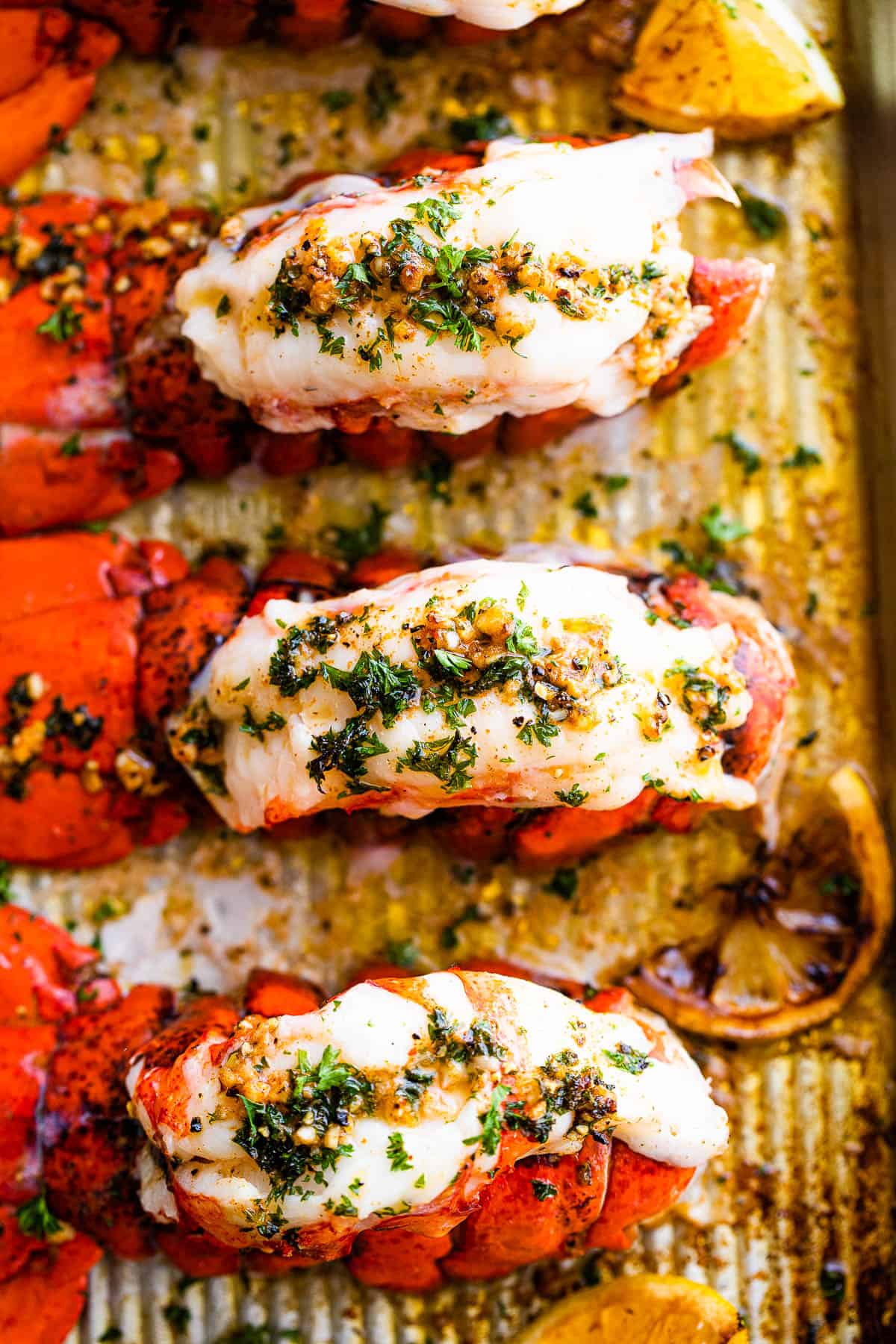 Three Baked Lobster Tails on a Pan Topped with Butter and Parsley