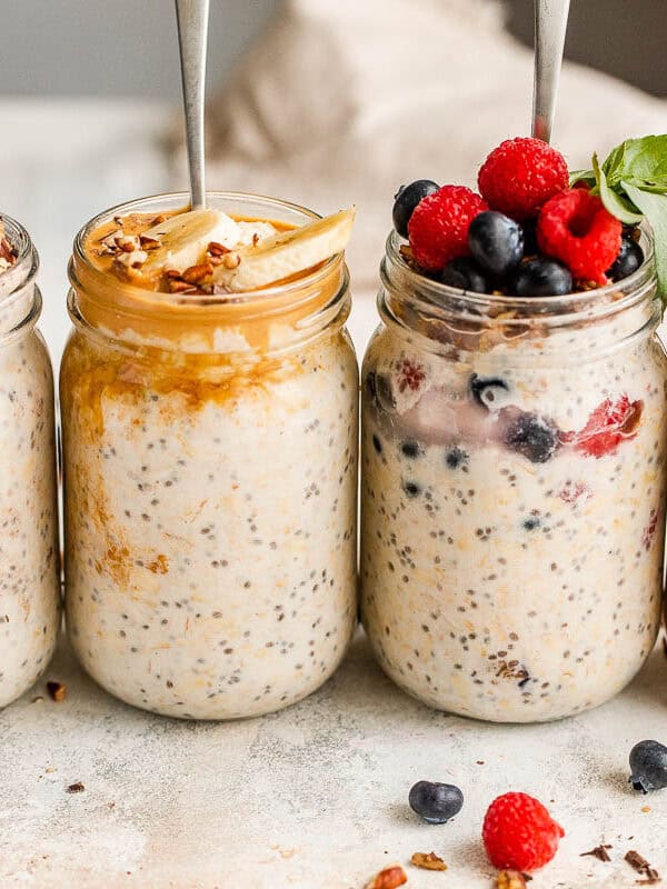 Four jars filled with oats and topped with fruits and granola.