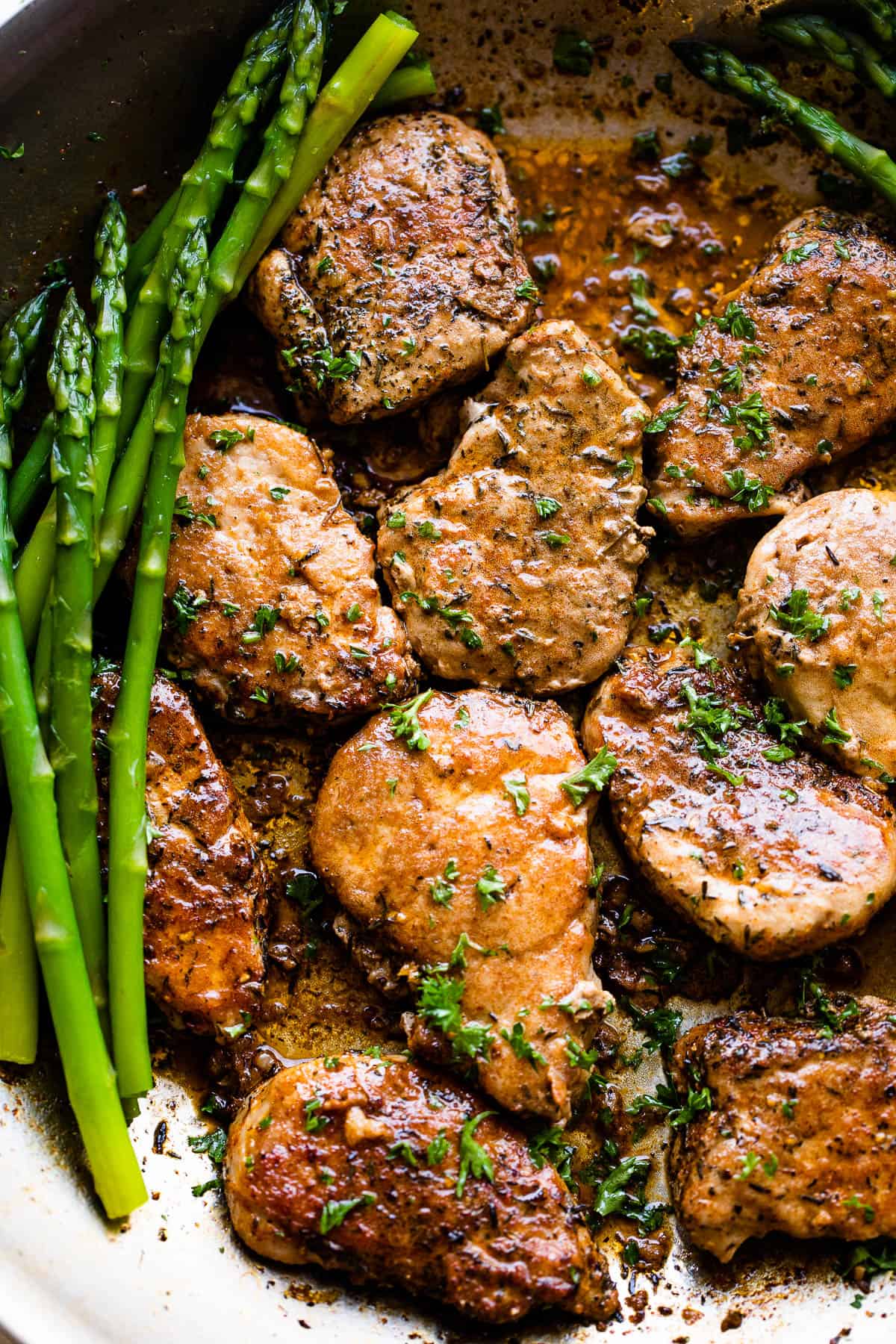 Pork medallions in a skillet with stalks of asparagus placed on either side of them.