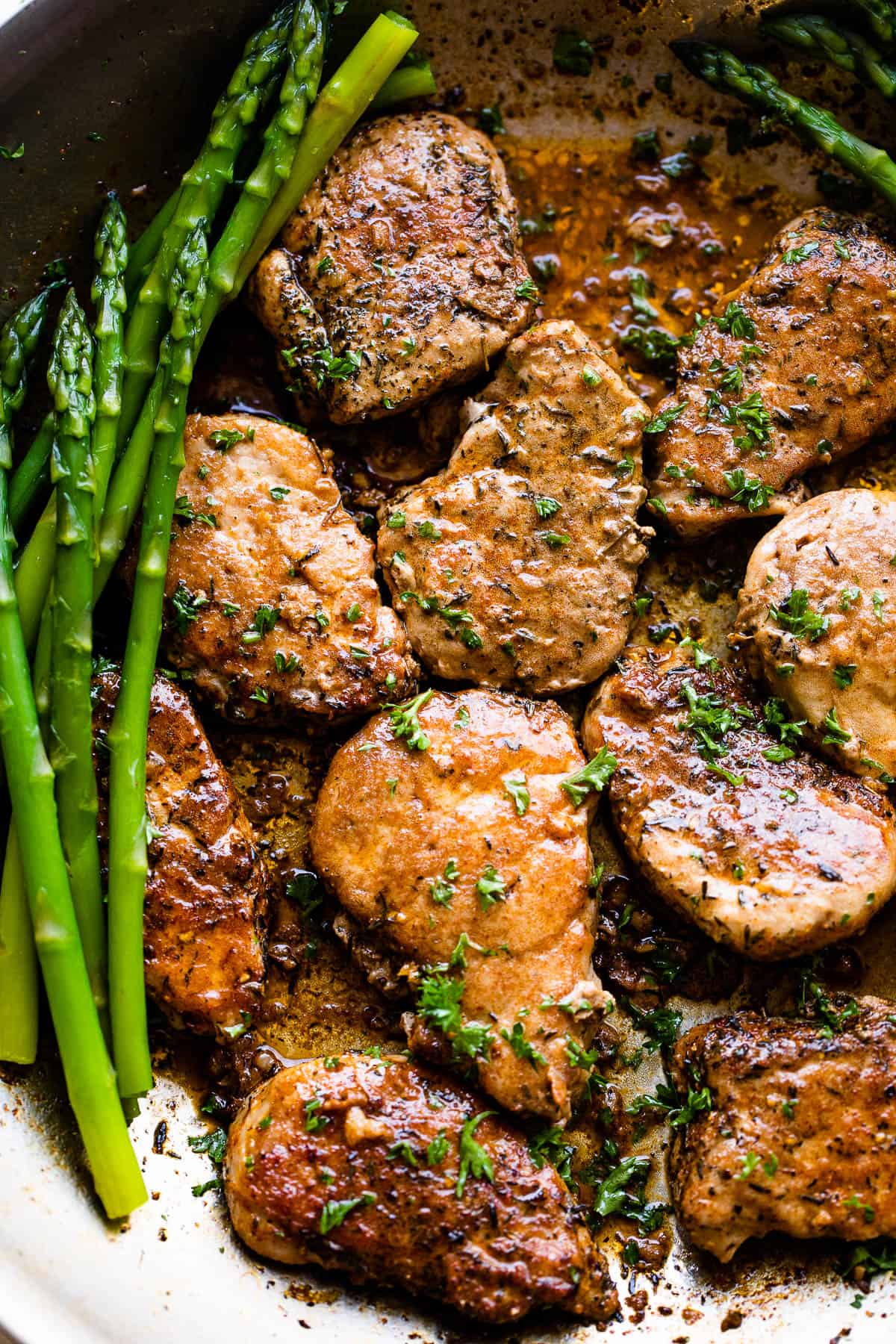 pork medallions in a skillet with stalks of asparagus to the side