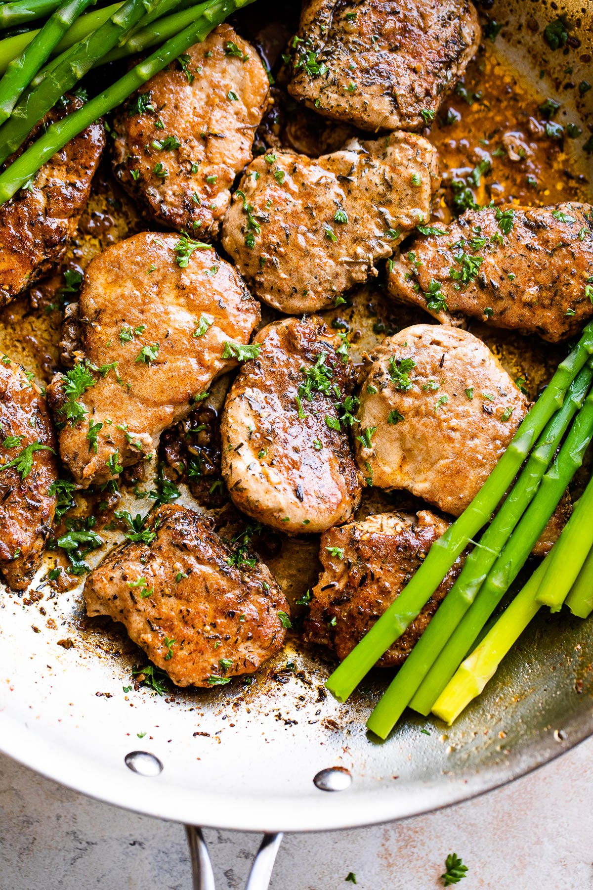 stainless skillet with pork medallions and asparagus