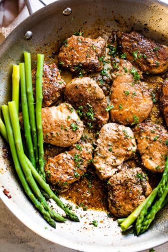 pork medallions in a skillet with stalks of asparagus to the side