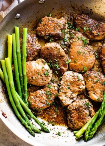 pork medallions in a skillet with stalks of asparagus to the side