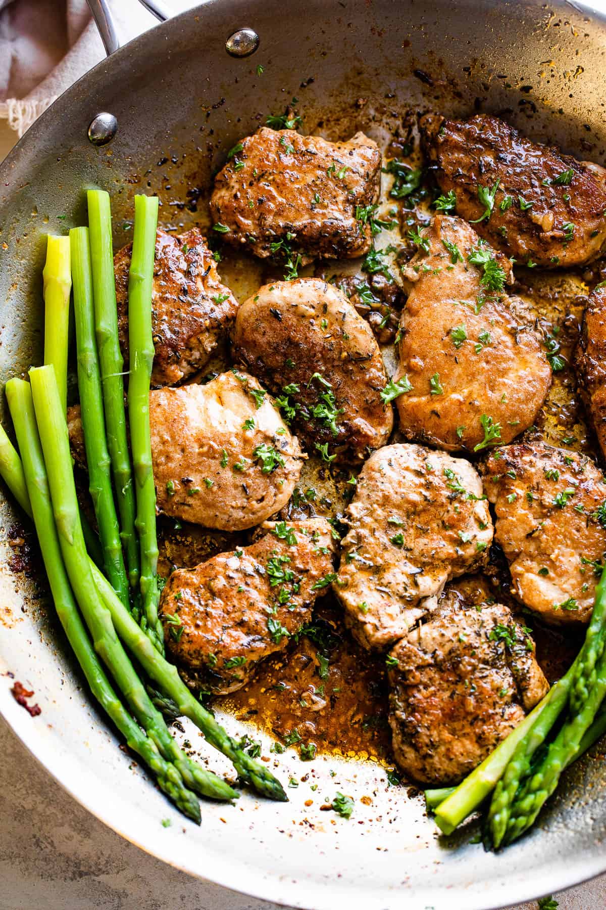 pork medallions in a skillet with stalks of asparagus to the side