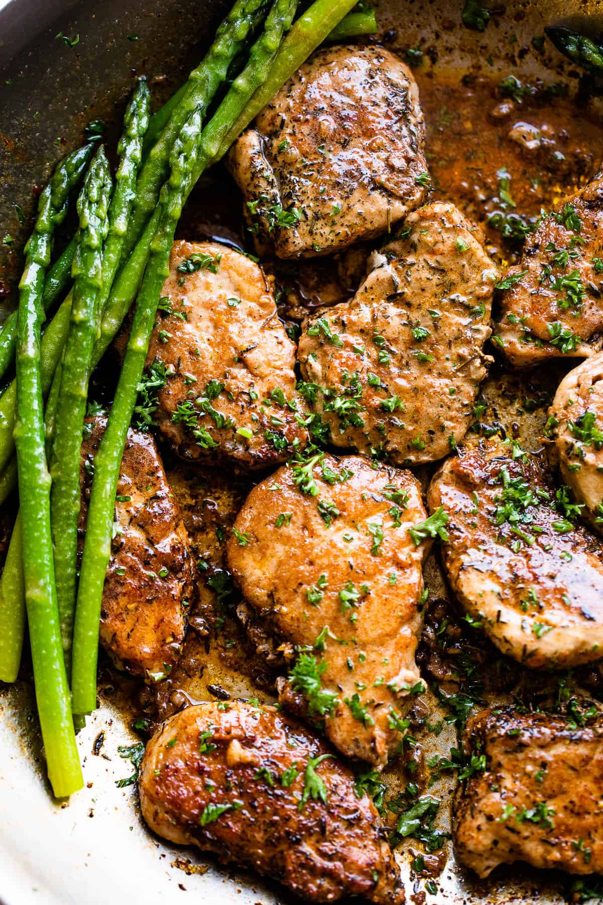 close up picture of pork medallions in a skillet with stalks of asparagus to the side