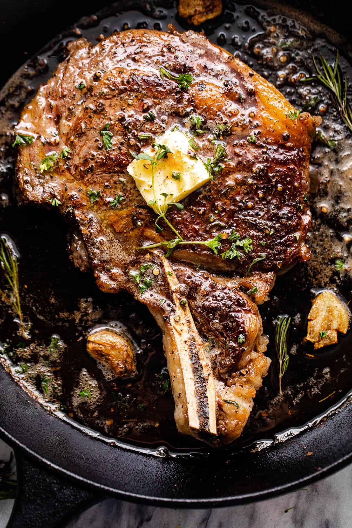 Overhead shot of a ribeye steak cooking in a cast iron skillet.