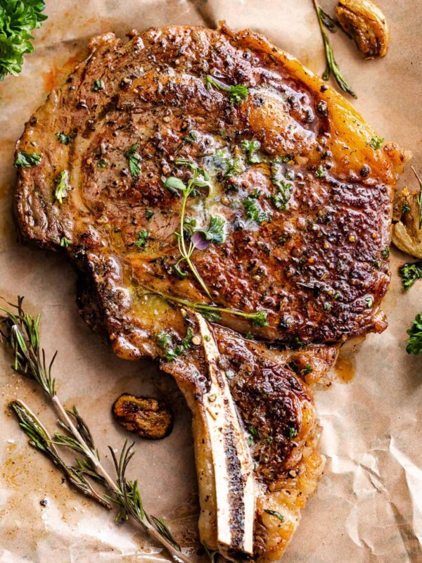 cooked ribeye steak placed on brown paper with garlic and parsley around it