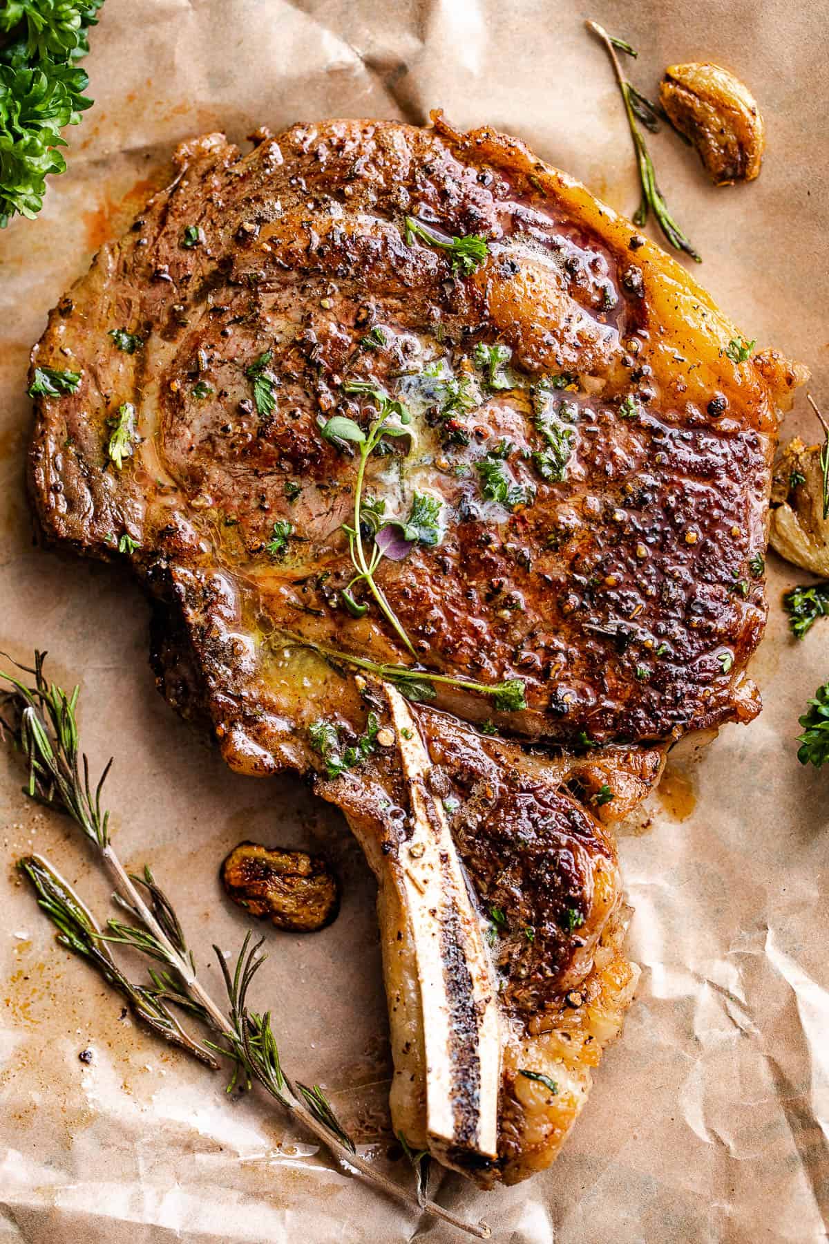 Cooked ribeye steak placed on brown paper with garlic and parsley around it.