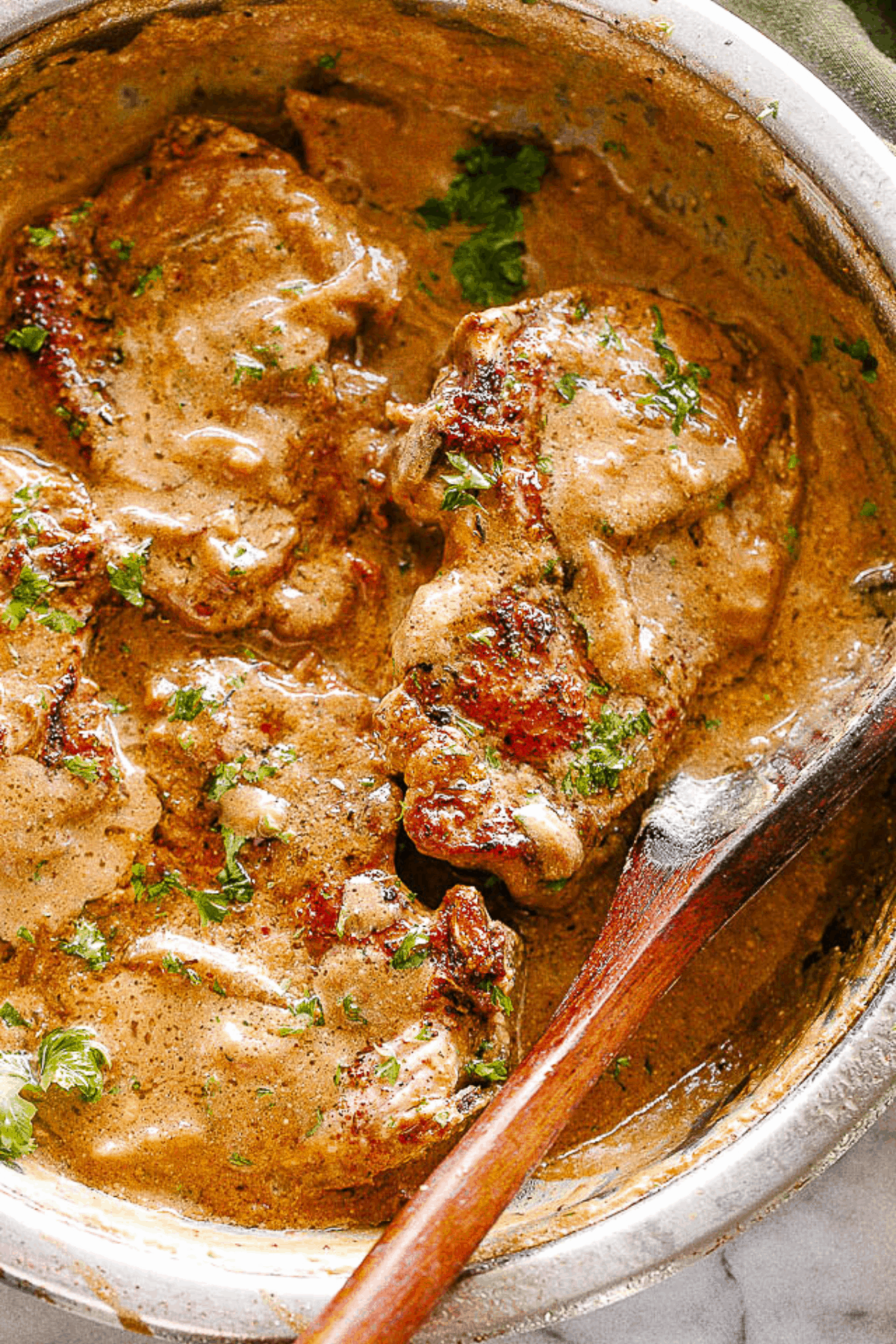 Smothered Pork Chops Overhead shot of smothered pork chops with onion gravy in a skillet.
