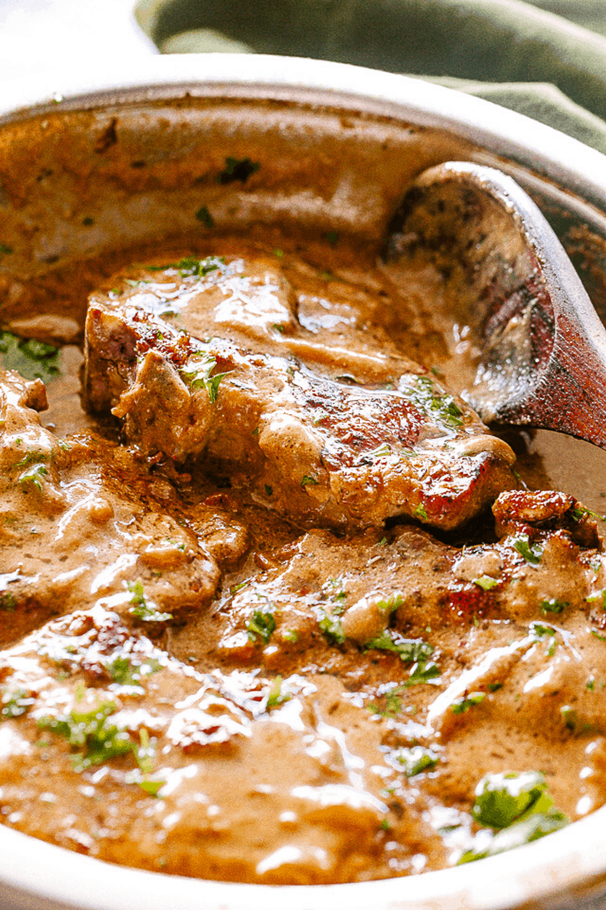 A stainless steel skillet with pork chops, gravy, and a wooden spoon.