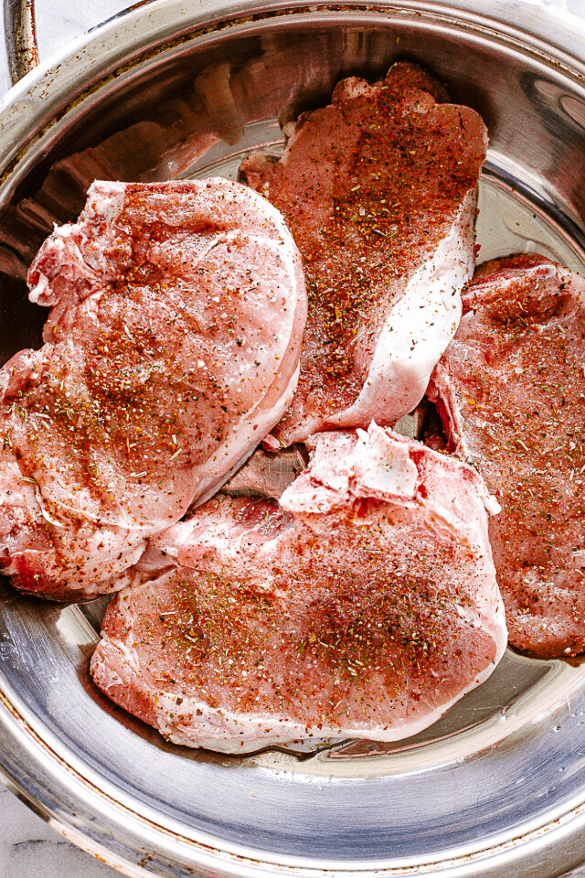 Raw pork chops sprinkled with seasoning, in a skillet.