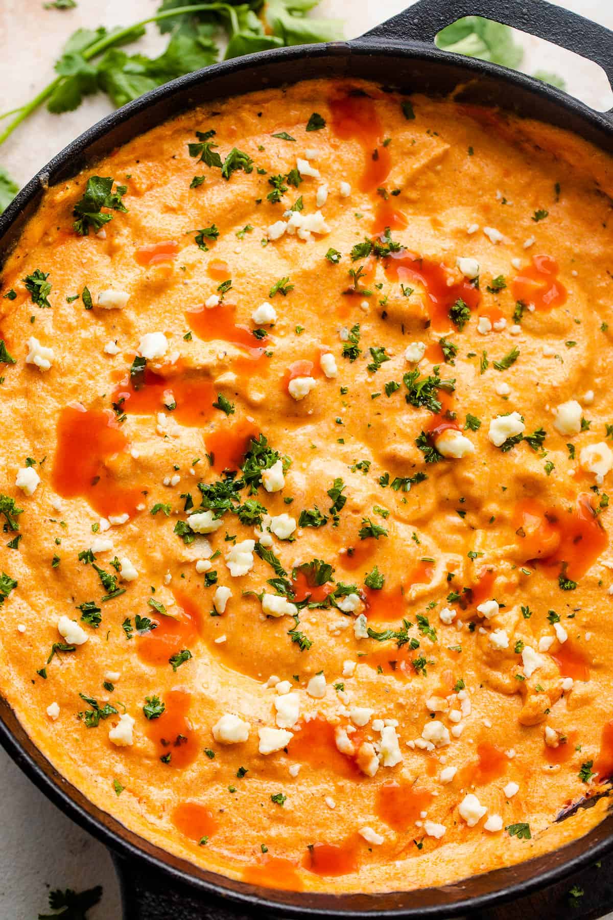 cast iron skillet with buffalo chicken dip garnished with parsley, hot sauce, and crumbled bleu cheese