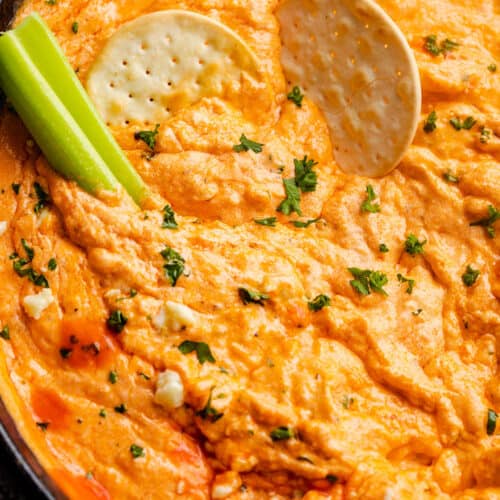 close up overhead shot of buffalo chicken dip in a cast iron skillet with two crackers and celery sticks in the dip