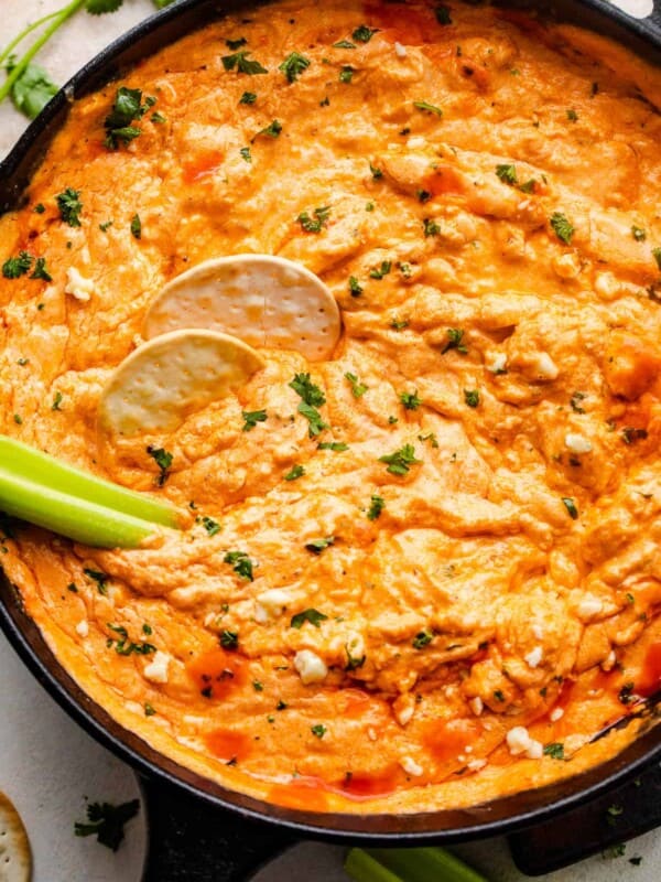 overhead shot of buffalo chicken dip in a cast iron skillet with two crackers and celery sticks in the dip