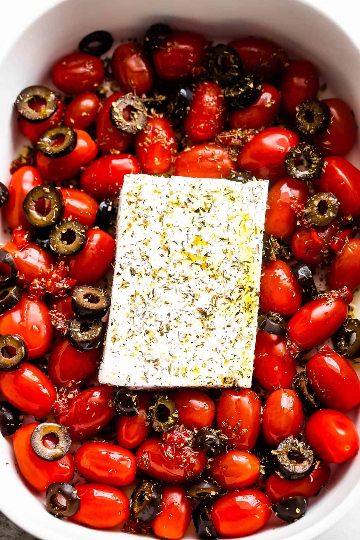 block of feta cheese surrounded by grape tomatoes and sliced olives