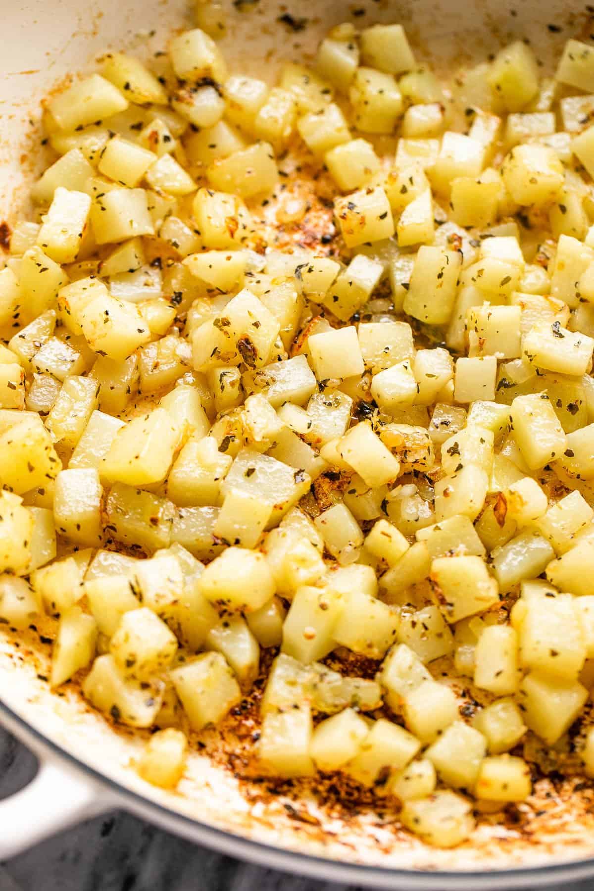 cooking diced potatoes in a white skillet