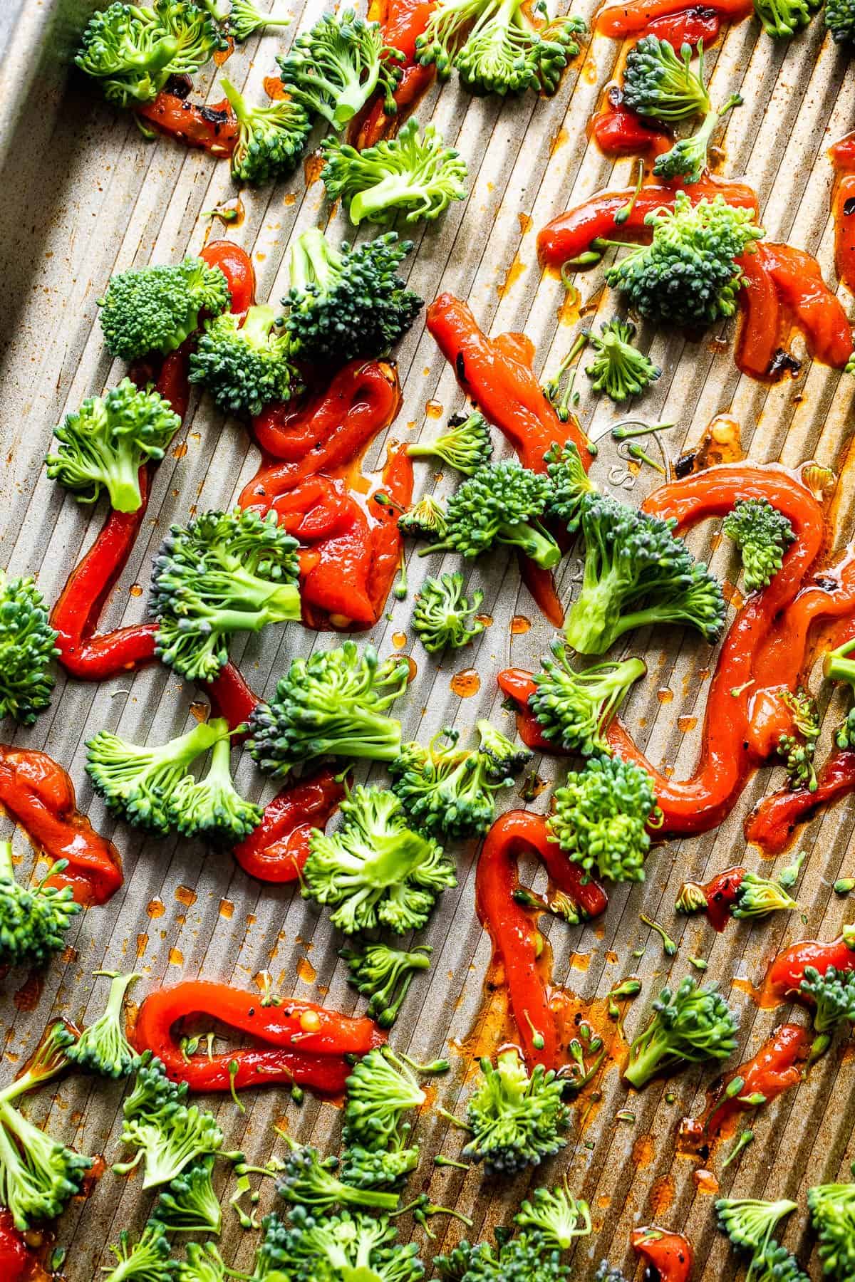 Broccoli florets and julienned red roasted peppers scattered on a baking sheet.