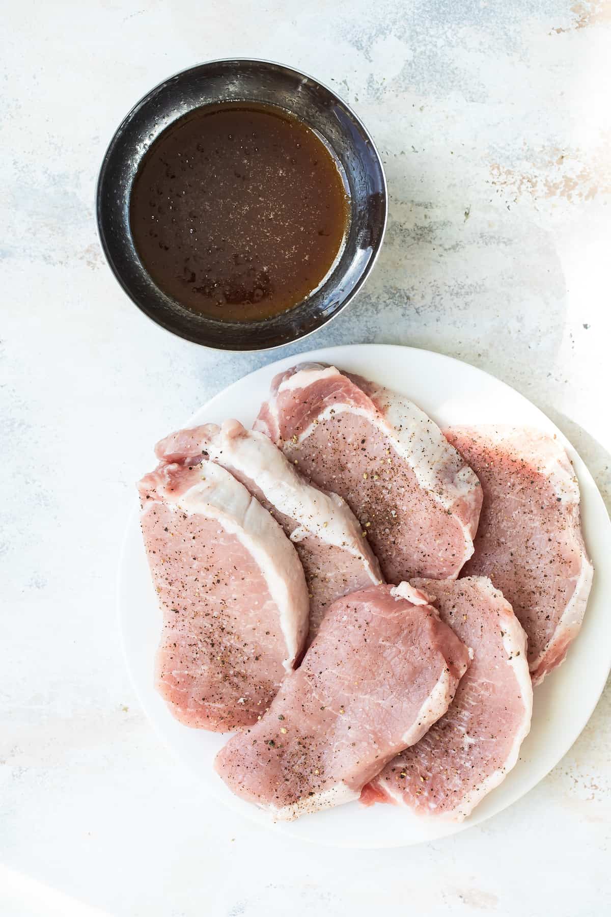 Seasoned Pork Chops on a Plate with a Dish of Marinade Beside Them