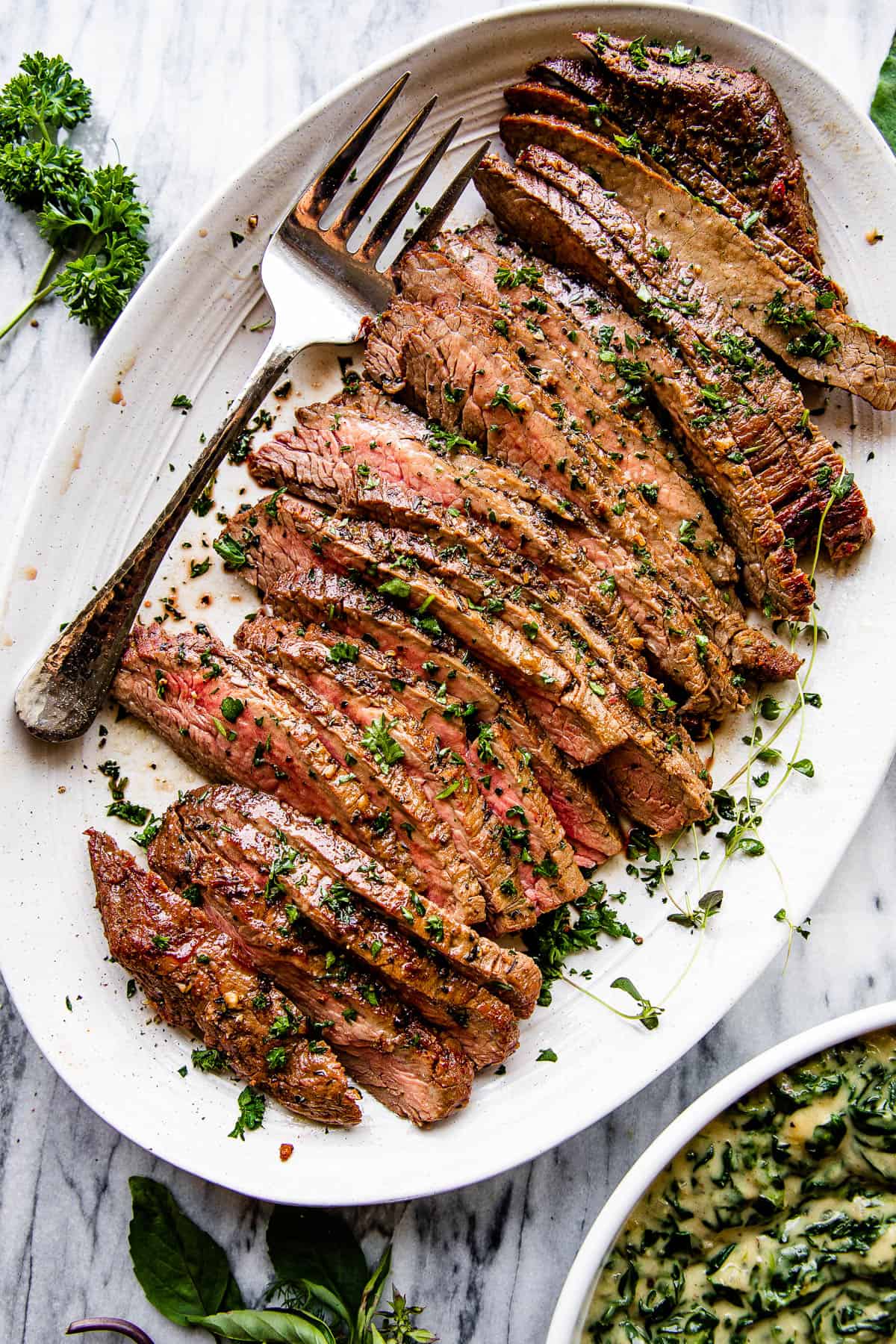 london broil sliced up and served on a platter with a serving fork on the side