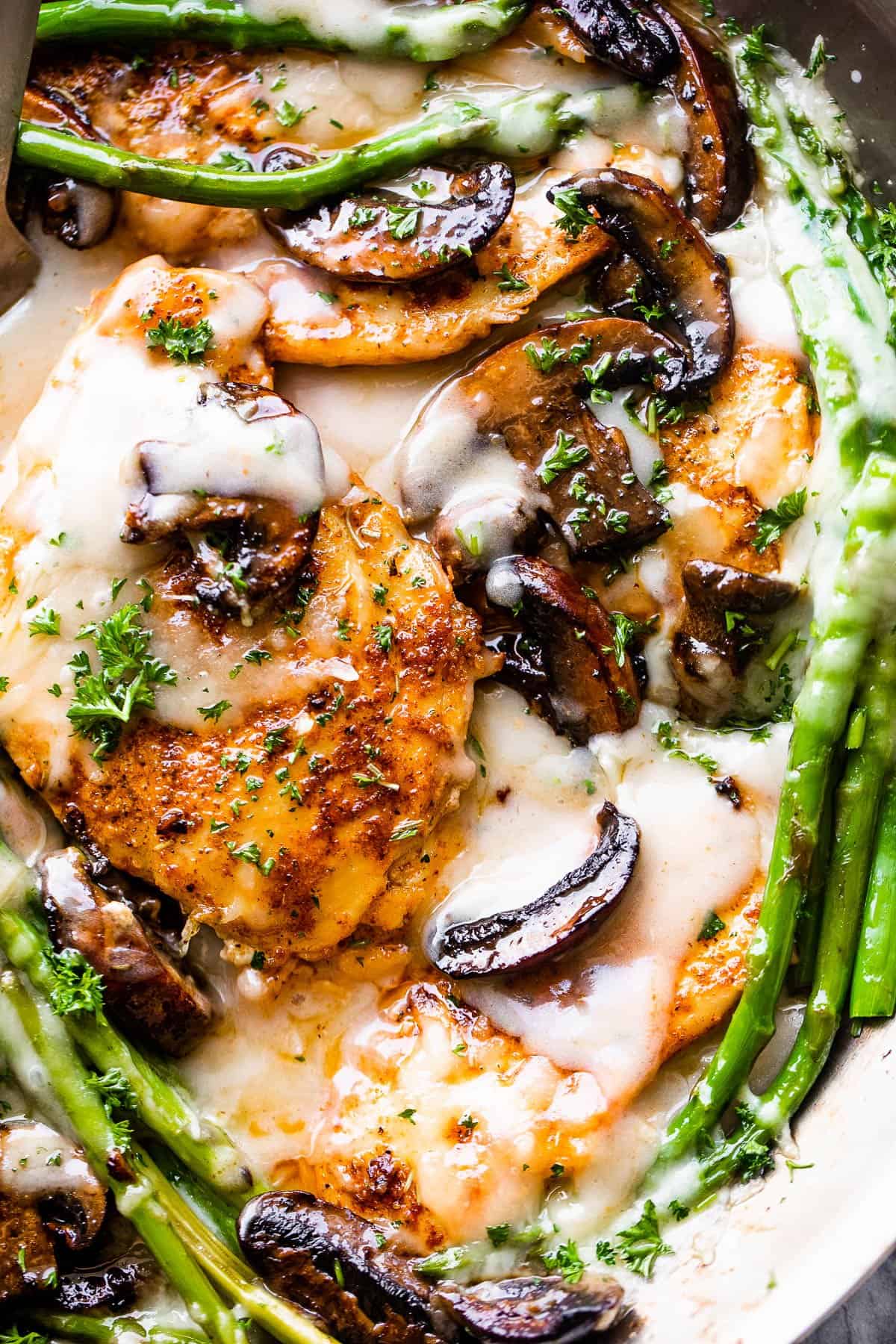 up close picture of chicken cutlets in madeira sauce topped with asparagus and mushrooms