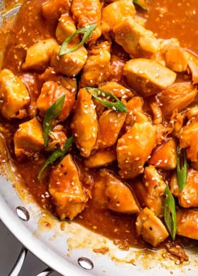 skillet with chicken bites in orange sauce and topped with sesame seeds and green onions