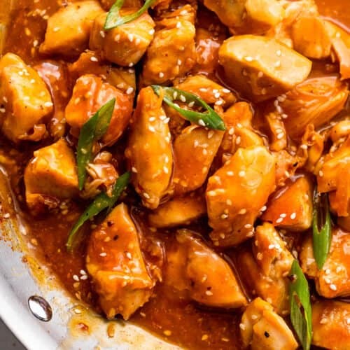 skillet with chicken bites in orange sauce and topped with sesame seeds and green onions