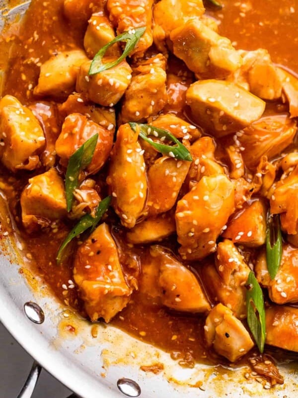 skillet with chicken bites in orange sauce and topped with sesame seeds and green onions