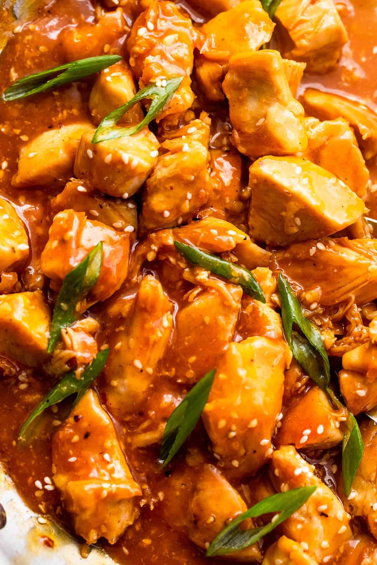 up close shot of chicken bites in orange sauce and topped with sesame seeds and green onions