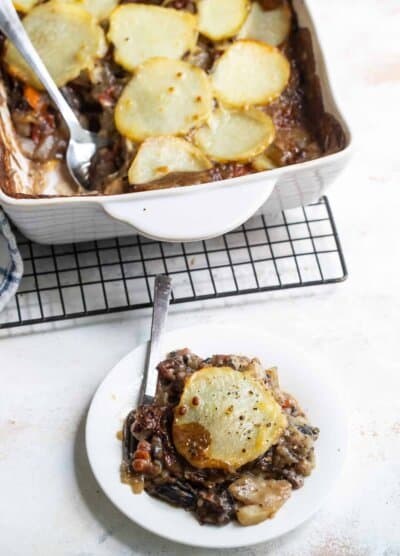 A Serving of Vegetable Moussaka on a Plate with a Pan of Moussaka Behind It